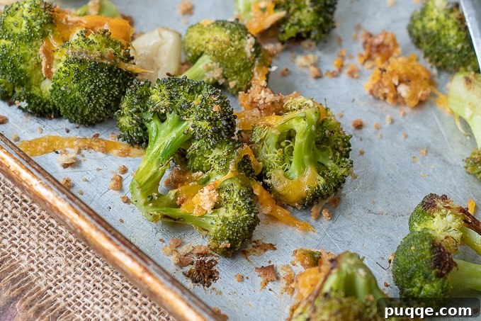A close-up of roasted broccoli and cheese on a baking sheet, showcasing the perfectly melted cheese and golden breadcrumbs.