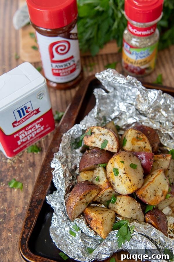 A foil packet of perfectly grilled potatoes resting on a baking sheet, with the McCormick and Lawry's seasonings used to prepare them displayed nearby.