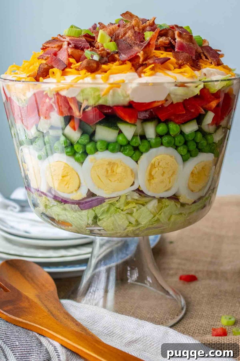 trifle bowl of 7 layer salad with wood serving utensils laying next to it