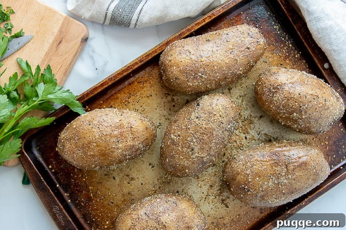 A baking sheet laden with several golden-brown Instant Pot baked potatoes, each boasting perfectly seasoned and crispy skins. Sprigs of fresh parsley are artfully arranged beside them.