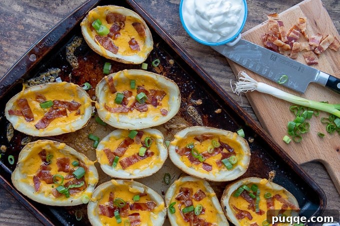 An overhead shot of an array of golden-brown loaded potato skins arranged neatly on a baking sheet, with small dishes of sour cream and freshly chopped green onions placed beside them, ready for serving.