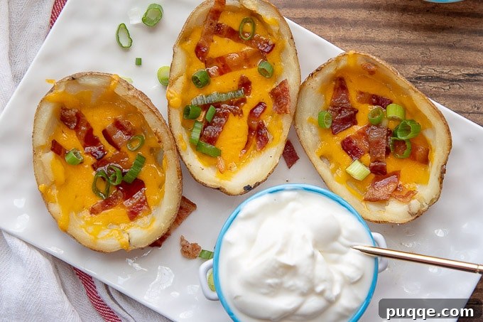 Three perfectly golden, deep-fried potato skins artfully arranged on a white rectangular plate, with a small dish of sour cream positioned elegantly in the center, inviting a delightful culinary experience.