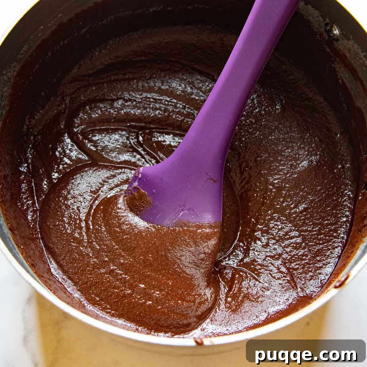 Perfectly Fudgy Gluten-Free Brownies with Crackly Tops 5 A purple spoon gently stirring a rich, melted chocolate mixture in a saucepan, creating a smooth brownie base.