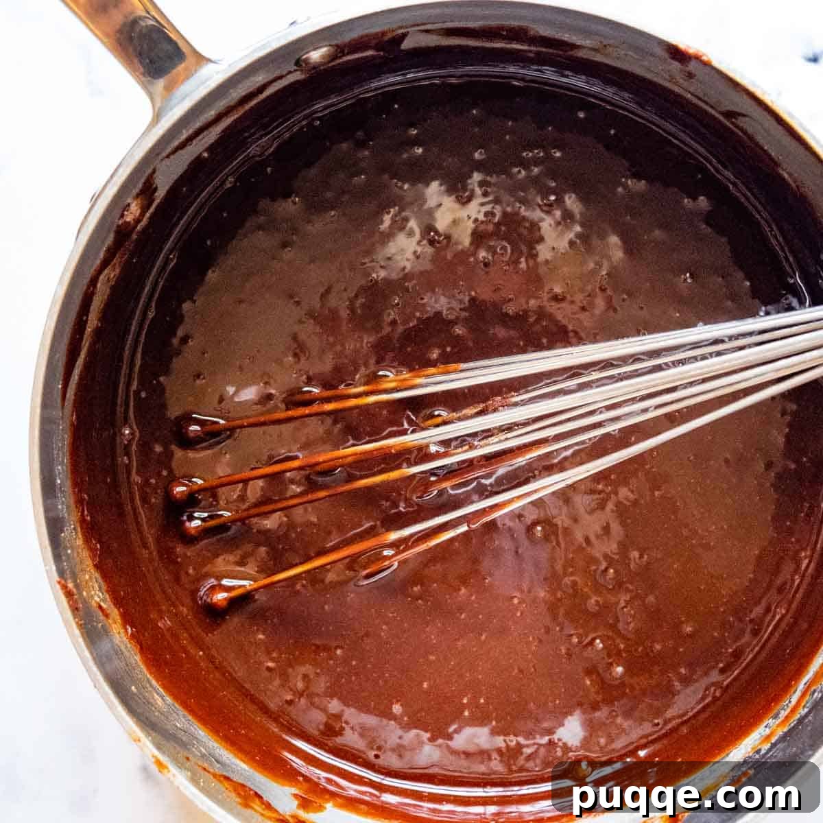 Perfectly Fudgy Gluten-Free Brownies with Crackly Tops 6 A whisk blending eggs and vanilla into the slightly cooled chocolate mixture in a saucepan, preparing for the next stage of brownie batter.