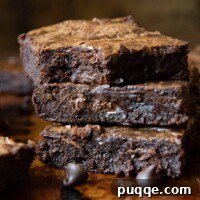 A stack of perfectly fudgy gluten-free brownies with a corner bitten off the top one, revealing its dense, moist interior.