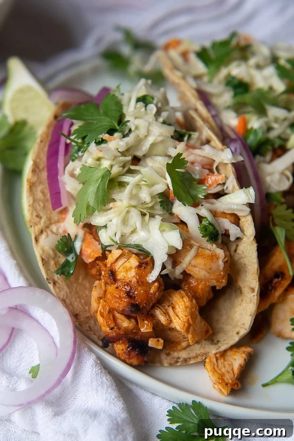 Close-up of Buffalo Chicken Tacos topped with creamy blue cheese slaw and sliced red onions on a white plate