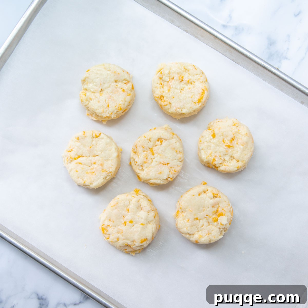 Melt-in-Your-Mouth Gluten-Free Cheddar Scones 8 Unbaked scones arranged close together on a parchment-lined baking sheet, ready for the oven.