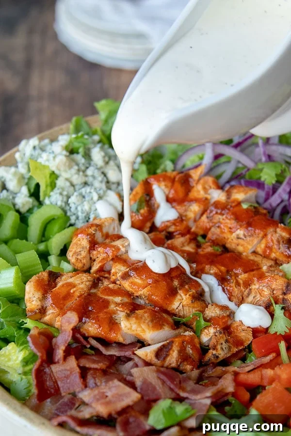 Ranch dressing being poured over a fresh Buffalo Chicken Salad in a rustic bowl.