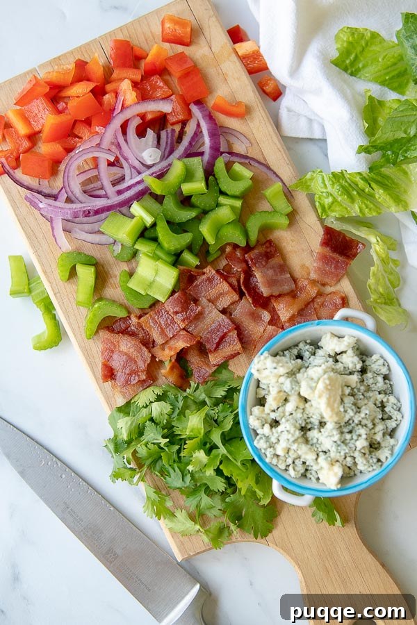 An overhead shot of a wooden cutting board displaying all the prepped, chopped ingredients for the Buffalo Chicken Salad.