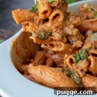 a serving spoon holding up a serving of pasta covered in sausage red sauce