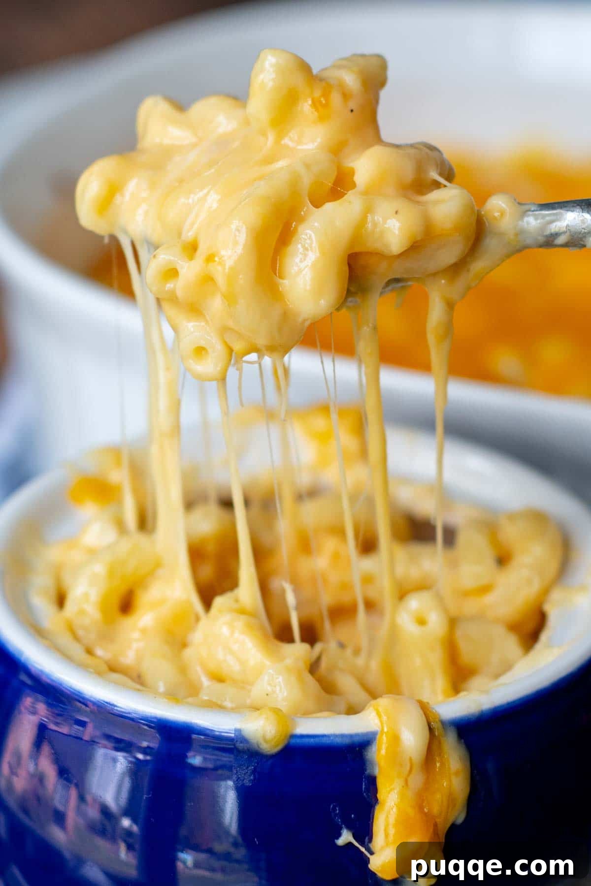 A spoon lifting a perfect bite of mac and cheese, showcasing the creamy sauce and tender pasta, from a vibrant blue bowl.