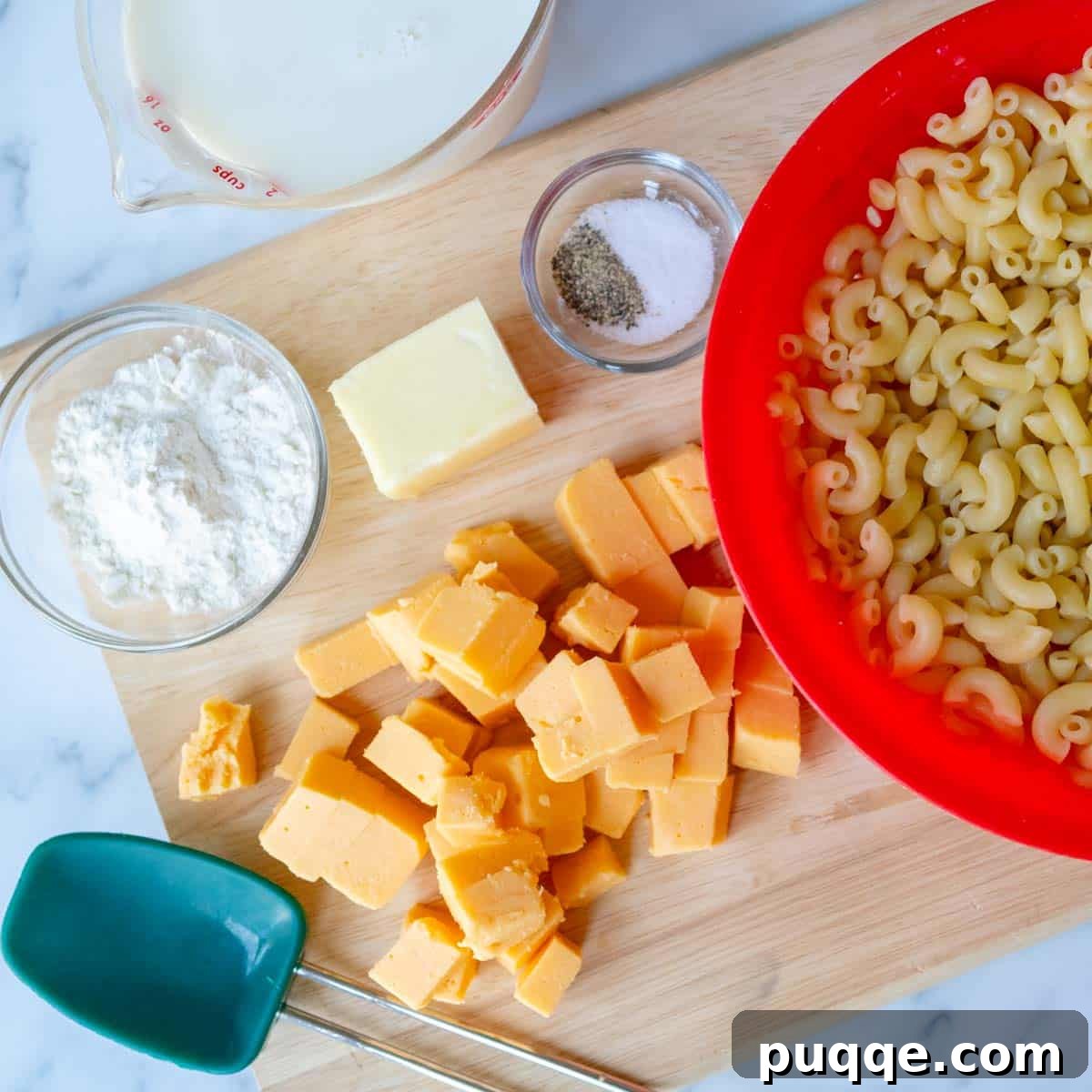 All the essential ingredients for baked mac and cheese—cubed Velveeta, elbow macaroni, butter, flour, milk, salt, and pepper—neatly prepped and arranged on a countertop.