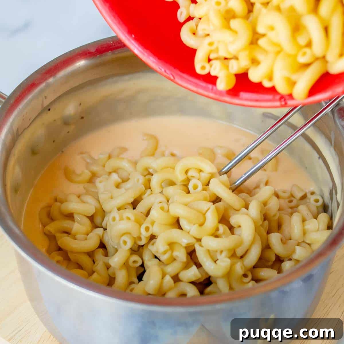 Cooked elbow pasta being gently added to the large saucepan filled with creamy Velveeta cheese sauce, ready for mixing.