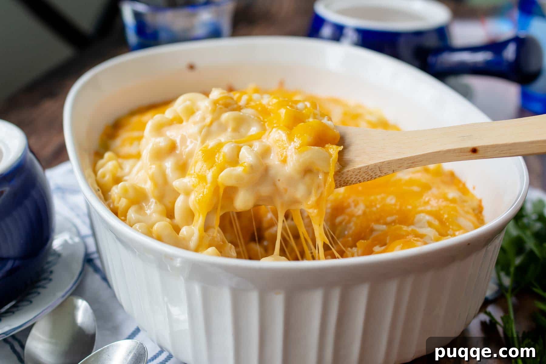 A casserole dish with a large wooden spoon scooping out a serving of hot, bubbly mac and cheese, showing its golden-brown topping and creamy interior.