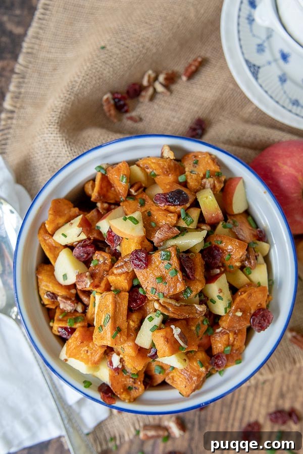 Orchard Sweet Potato Salad 2 Overhead shot of vibrant roasted sweet potato salad with a serving spoon, garnished with fresh apple slices and parsley, showcasing its rich textures and inviting colors.