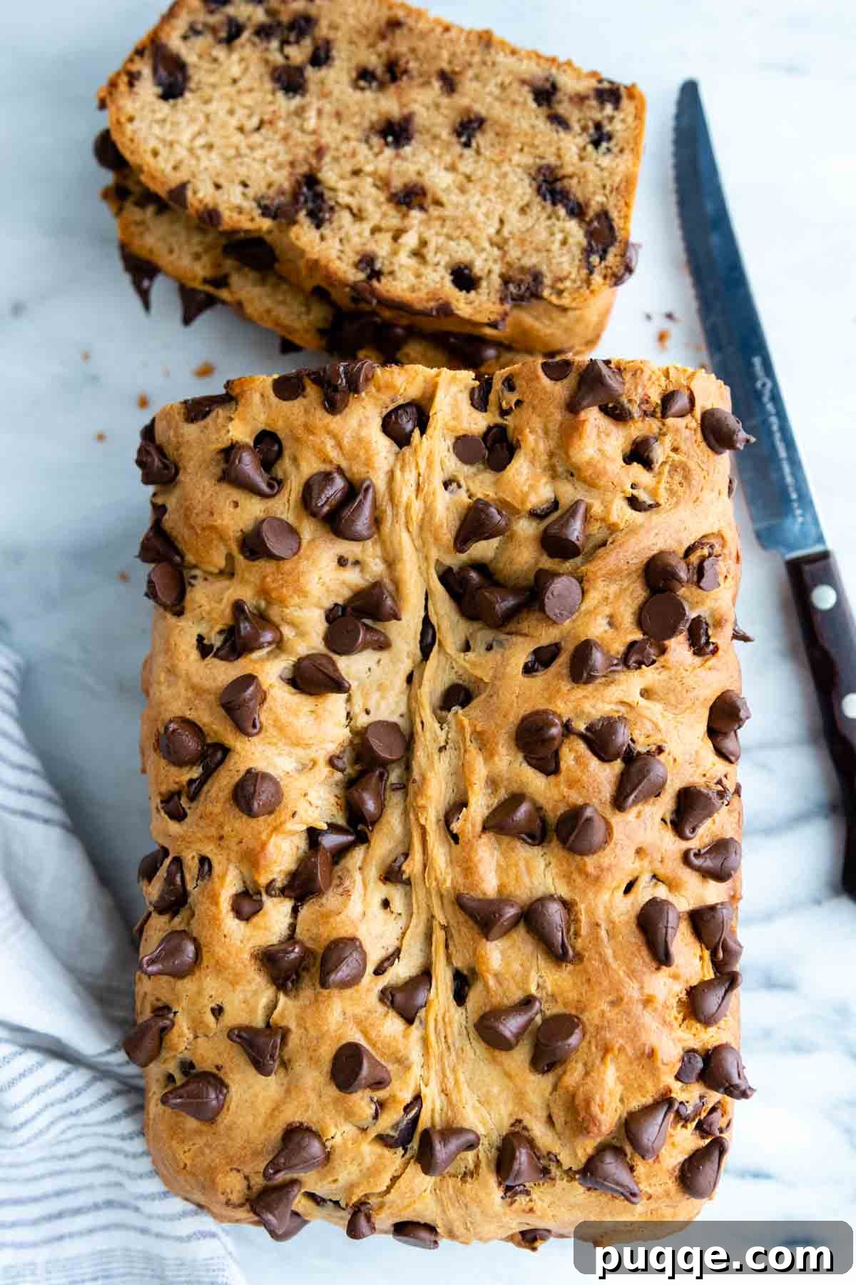 Effortless Gluten-Free Peanut Butter Quick Bread 6 Overhead view of a delicious gluten-free peanut butter bread loaf with melted chocolate chips on a white surface, invitingly ready to be sliced.