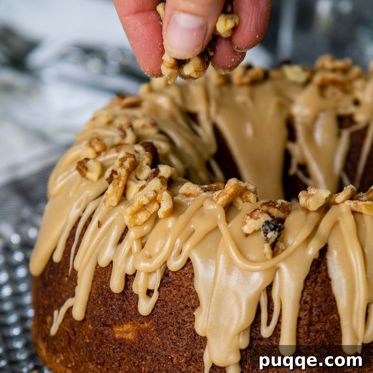 Brown Sugar Praline Glazed Apple Cake 12 Chopped walnuts being sprinkled over the still-wet brown sugar glaze on an apple cake.