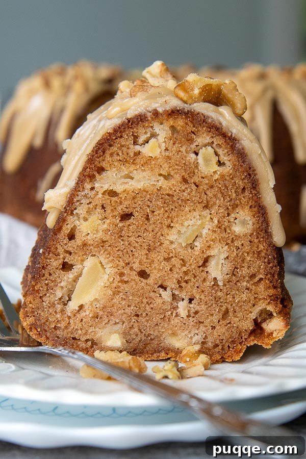 Brown Sugar Praline Glazed Apple Cake 13 A close-up shot of a thick slice of moist apple cake, standing upright on a small white plate, showing off its tender crumb and rich praline glaze.