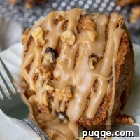 A slice of fresh apple cake on a white plate with brown sugar glaze and walnuts drizzled all over