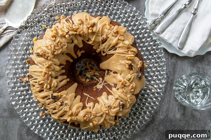 Brown Sugar Praline Glazed Apple Cake 3 An inviting overhead view of a moist apple bundt cake, generously coated with glistening brown sugar praline glaze and sprinkled with chopped nuts, fresh from the oven and ready to be served.