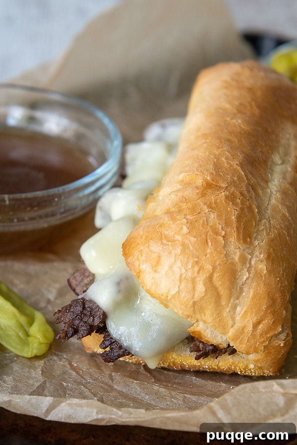 A French Dip sandwich resting on a baking sheet, accompanied by a cup of beef broth for dipping