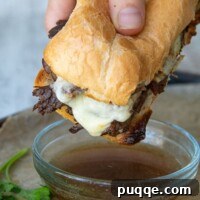 A hand holding French Dip sandwich about to be dipped into au jus