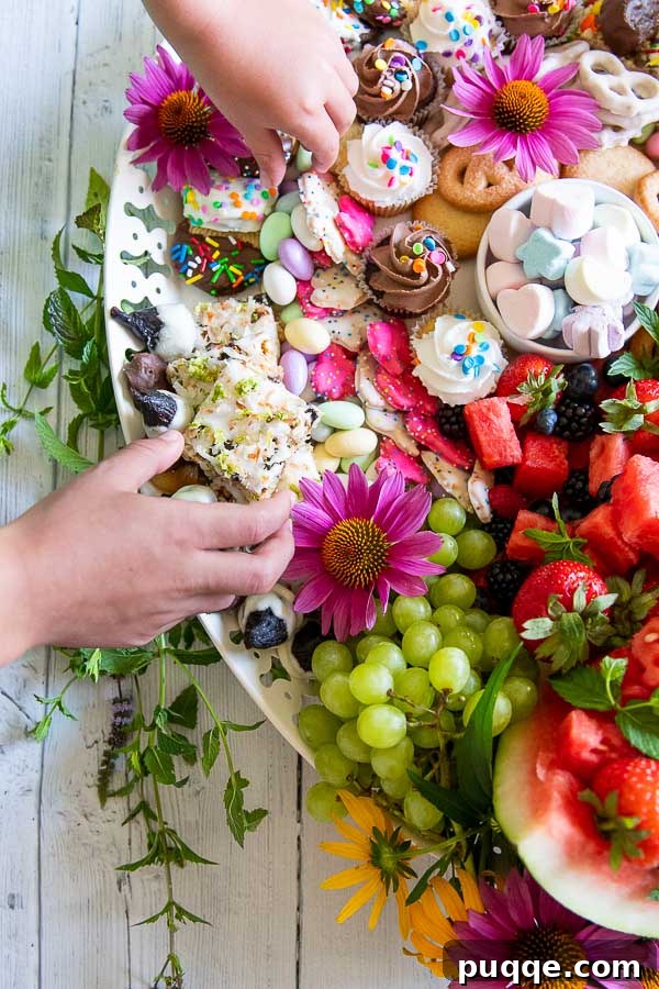 A child's hand reaches playfully towards a sweet treat on a bountiful dessert charcuterie board, highlighting the irresistible allure for all ages.