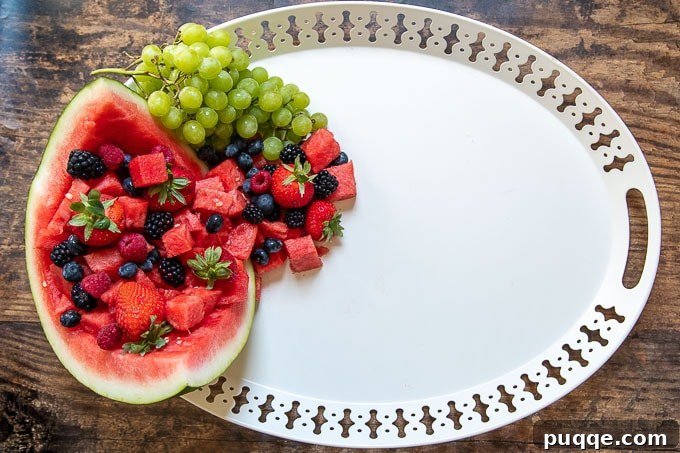 The second step in creating a dessert platter is filling the hollowed-out watermelon with a vibrant assortment of fresh fruit.