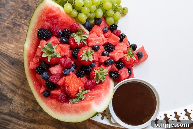 A close-up shot of the dessert board shows a hollowed watermelon filled with fruit, next to a small cup of melted chocolate, illustrating the third step of arrangement.