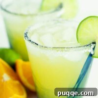 two glasses of skinny margarita with sliced oranges and limes lying next to them