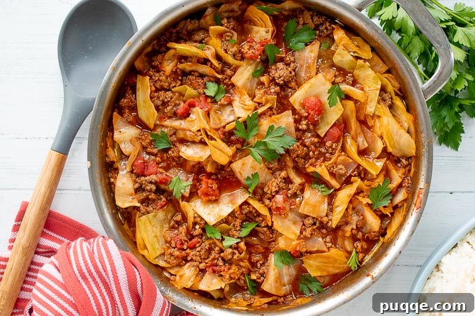 Overhead view of savory unstuffed cabbage rolls simmering in a large skillet, with a wooden spoon and kitchen towel beside it.