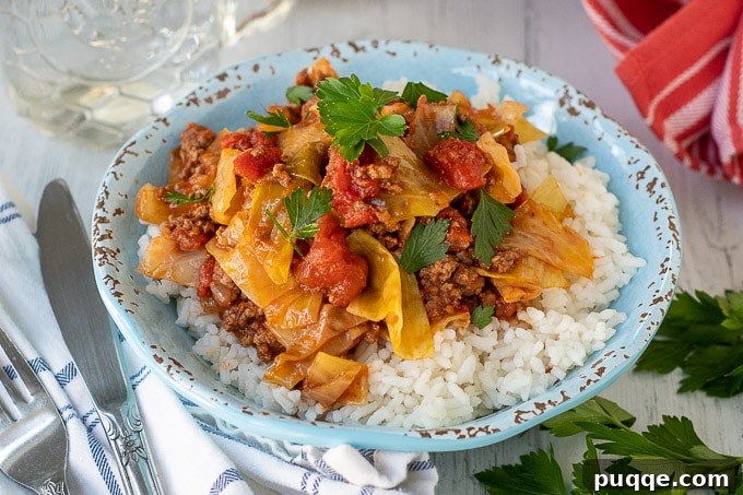 A close-up of a blue bowl filled with generous serving of unstuffed cabbage rolls, perfectly portioned over fluffy white rice, ready to be enjoyed.