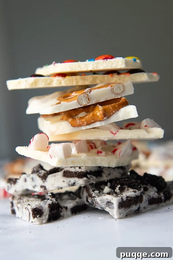 A beautifully arranged stack of various white chocolate barks, including Oreo, peppermint, pretzel, and festive Christmas-themed versions, showcasing their delicious textures and toppings.