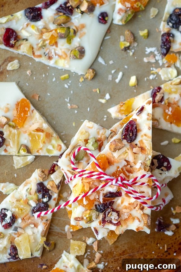 A close-up of fruit and nut white chocolate bark on a baking sheet, with a rustic string tied around a piece, suggesting it's ready for gifting or enjoying.