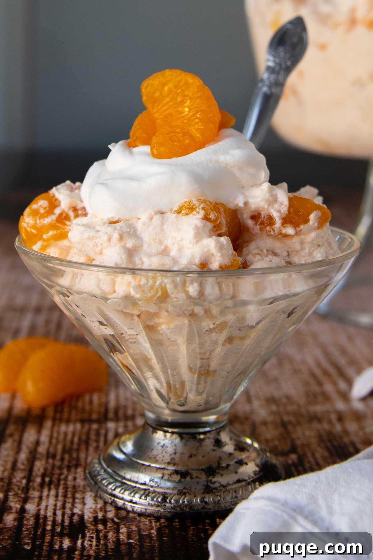 Mandarin Orange Cloud Delight 2 A beautifully presented orange jello salad in an old-fashioned serving dish, garnished with a fresh mandarin orange segment on top.
