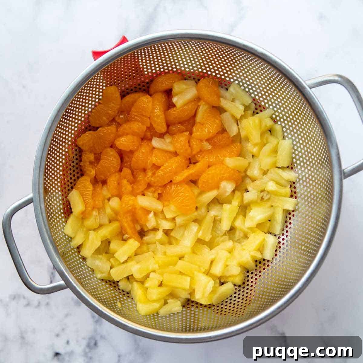 Mandarin Orange Cloud Delight 3 Well-drained fruit, including mandarin oranges and pineapple tidbits, resting in a colander over a bowl.