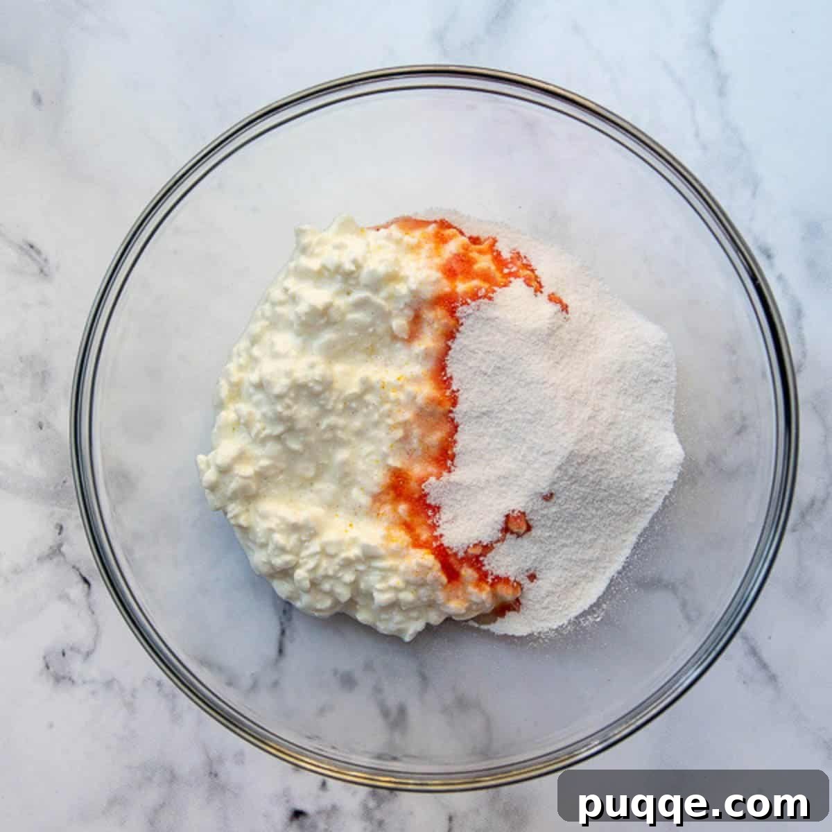 Mandarin Orange Cloud Delight 4 Orange jello powder being dissolved into small curd cottage cheese in a mixing bowl.