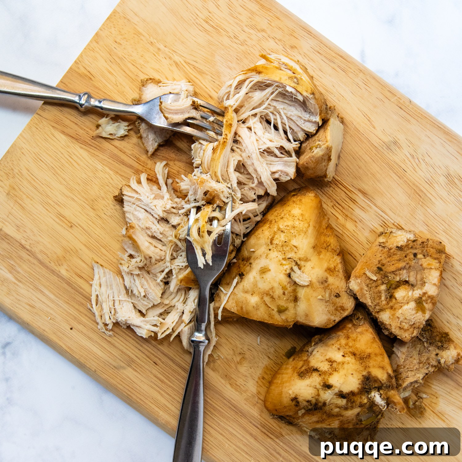 Gluten-Free White Chicken Chili The Secret to Its Deliciousness 4 Close-up shot of chicken breasts being shredded with two forks on a cutting board.