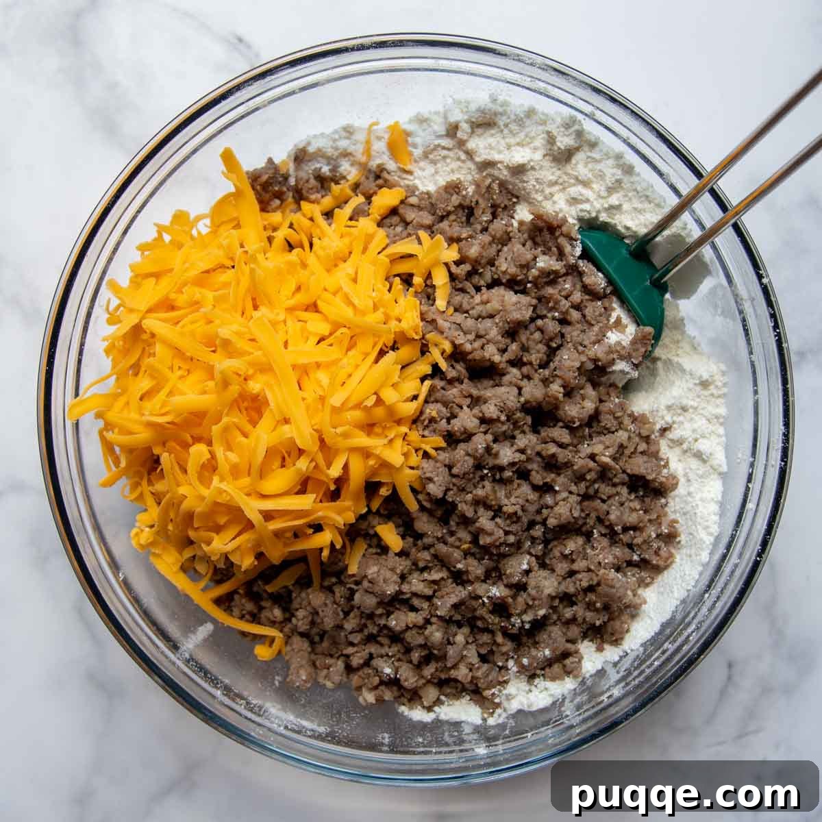 Sausage Cheddar Muffins 5 Cooked sausage and shredded cheddar cheese being added to the dry muffin mixture in a large mixing bowl, awaiting the wet ingredients.