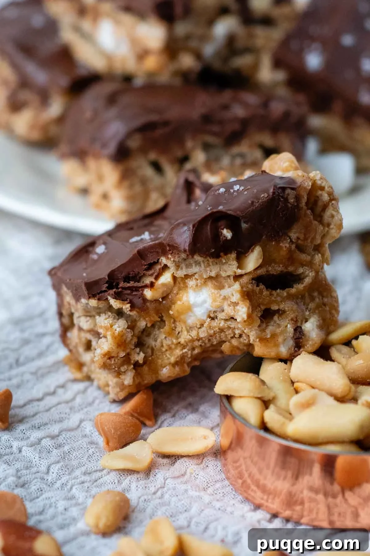 A perfectly portioned Scotcheroo bar with a bite taken out, revealing its soft, gooey interior of crispy cereal, peanuts, and melted marshmallows coated in peanut butter, topped with a smooth layer of butterscotch chocolate, facing the camera.