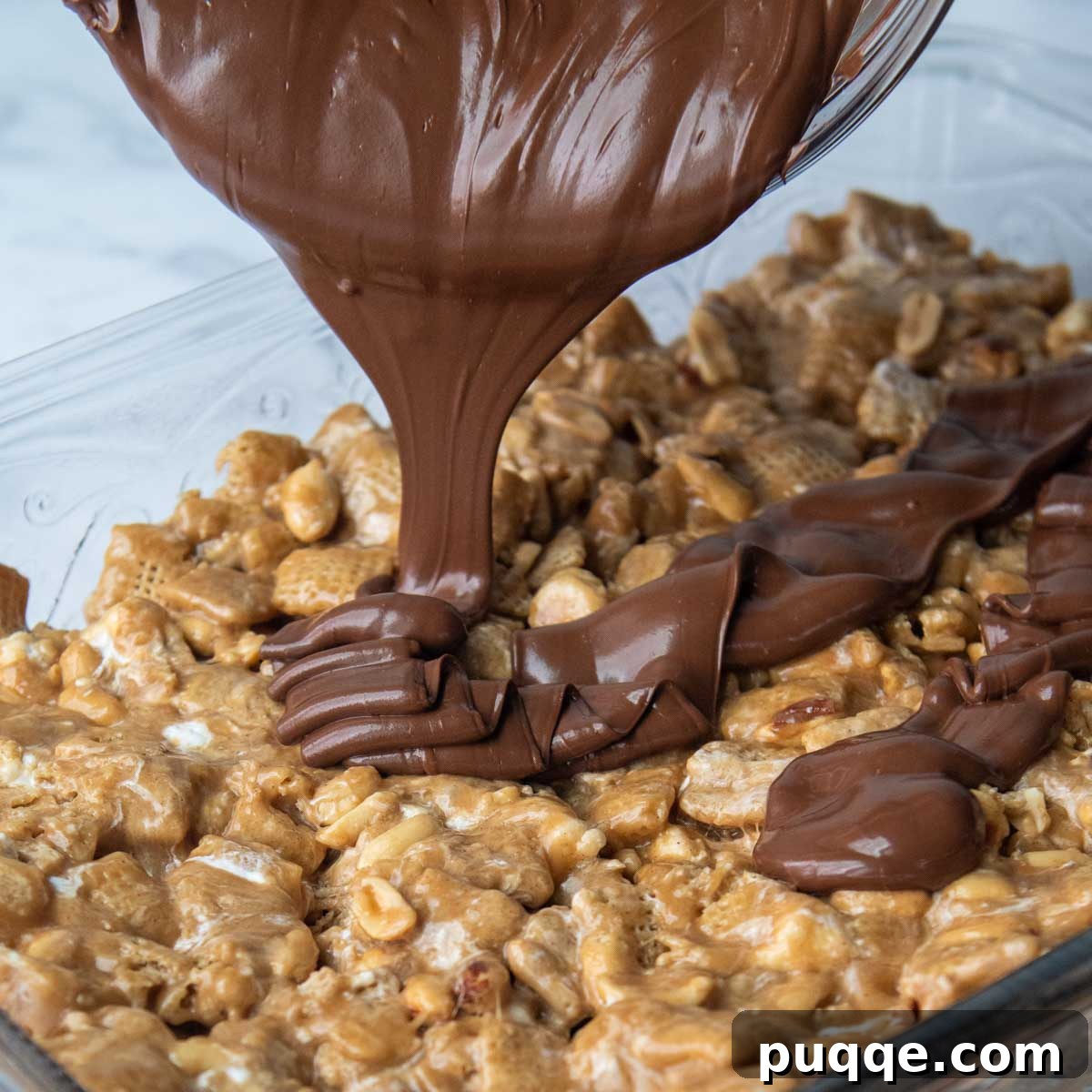 A thick layer of melted chocolate and butterscotch mixture being smoothly poured over the evenly spread Chex bars in a baking dish, ready to be spread.