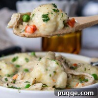 A wooden spoon holding up a scoop of chicken and dumplings