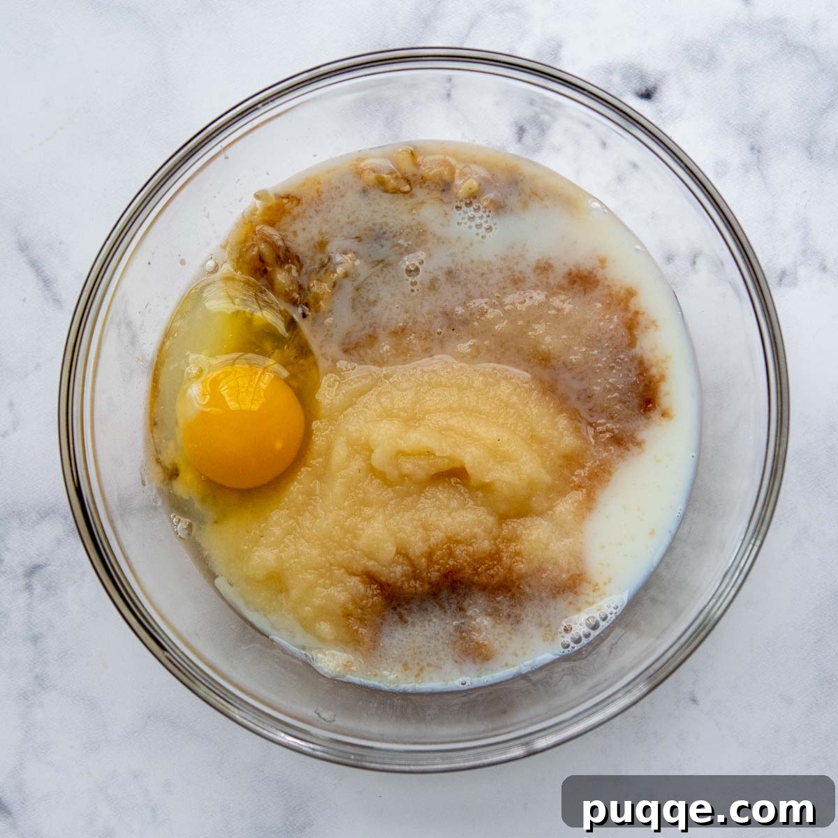 Wholesome Applesauce Oat Muffins 4 Wet ingredients including applesauce, mashed banana, and egg whisked in a separate bowl.