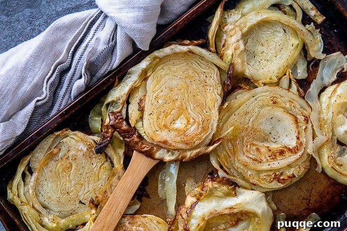 Golden Crispy Cabbage Steaks 5 A wooden spatula lifting a crispy, golden roasted cabbage slice from a sheet pan, showcasing its tenderness and caramelized edges.