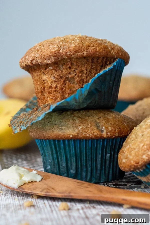 Perfectly Tender Gluten-Free Banana Muffins 2 A stack of two perfectly baked gluten-free banana muffins with a blue paper liner peeling off one, showcasing their fluffy texture.