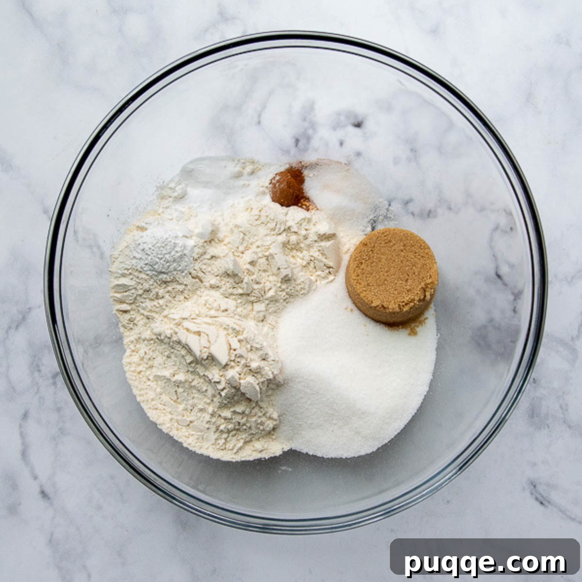 Perfectly Tender Gluten-Free Banana Muffins 3 The dry ingredients for gluten-free banana muffins, including flour, sugars, and spices, mixed together in a clear glass bowl.