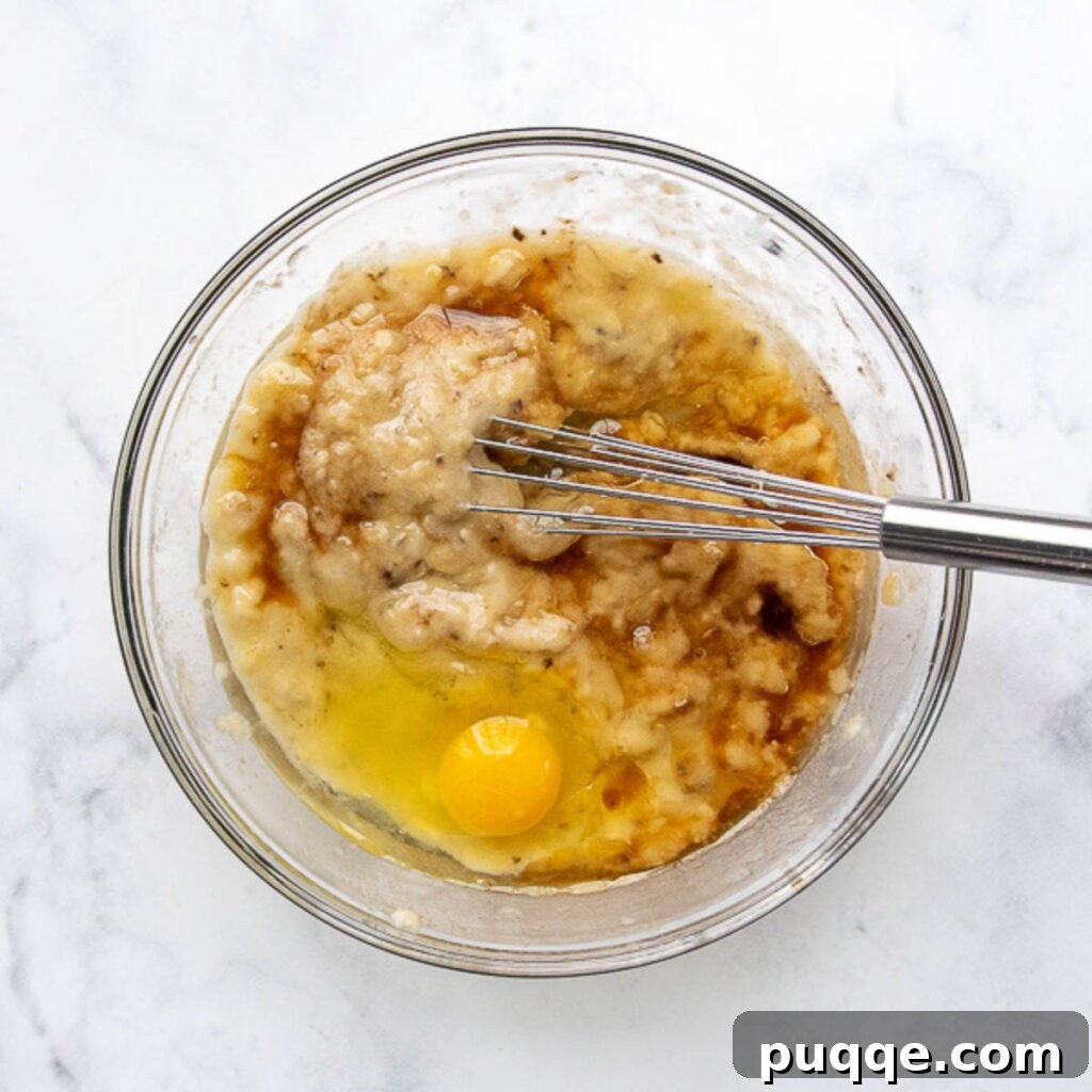 Perfectly Tender Gluten-Free Banana Muffins 4 Mashed ripe bananas being whisked with egg, oil, and vanilla extract in a bowl, preparing the wet ingredients for gluten-free muffins.