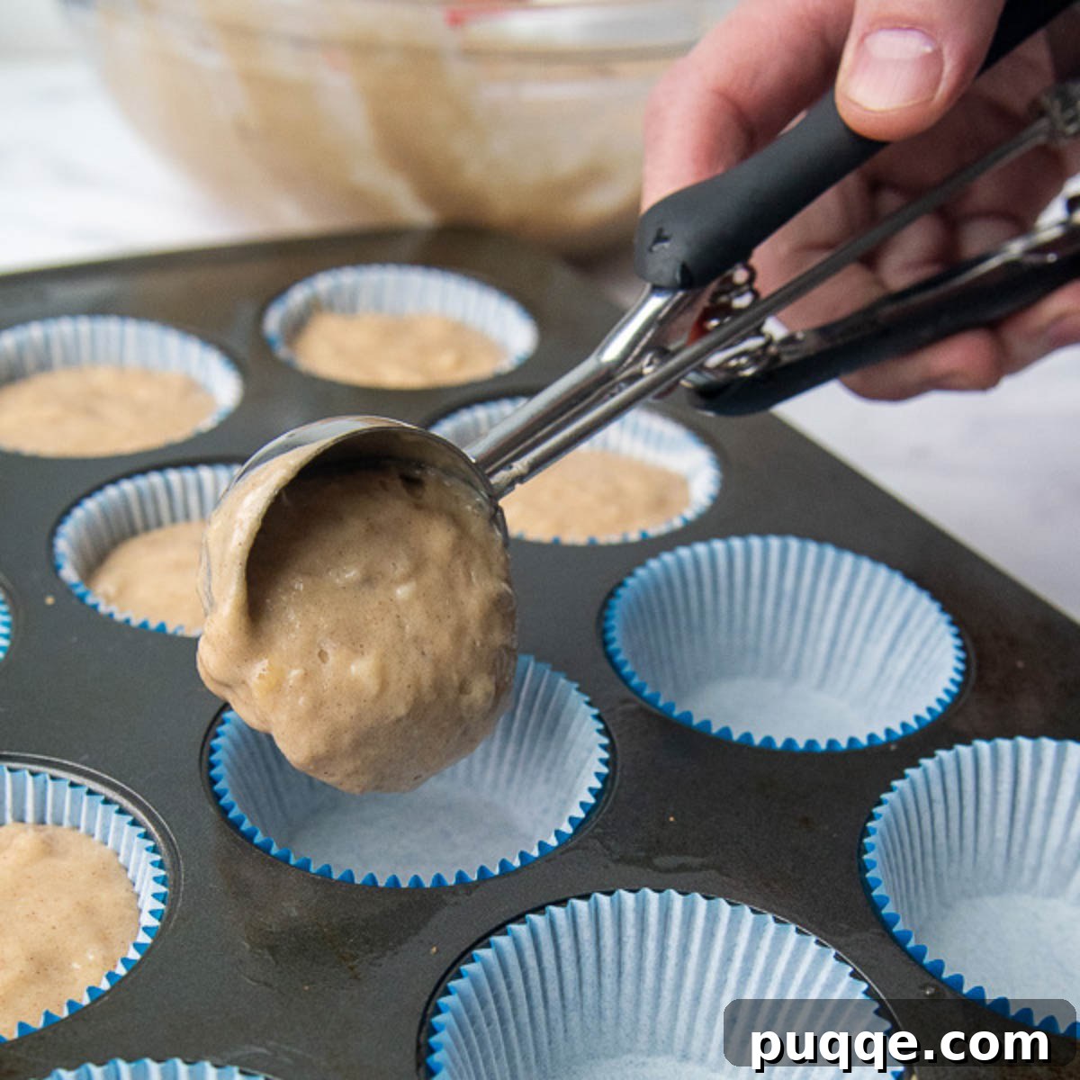 Perfectly Tender Gluten-Free Banana Muffins 5 A scoop of gluten-free banana muffin batter being perfectly portioned into a paper-lined muffin cup in a baking tin.