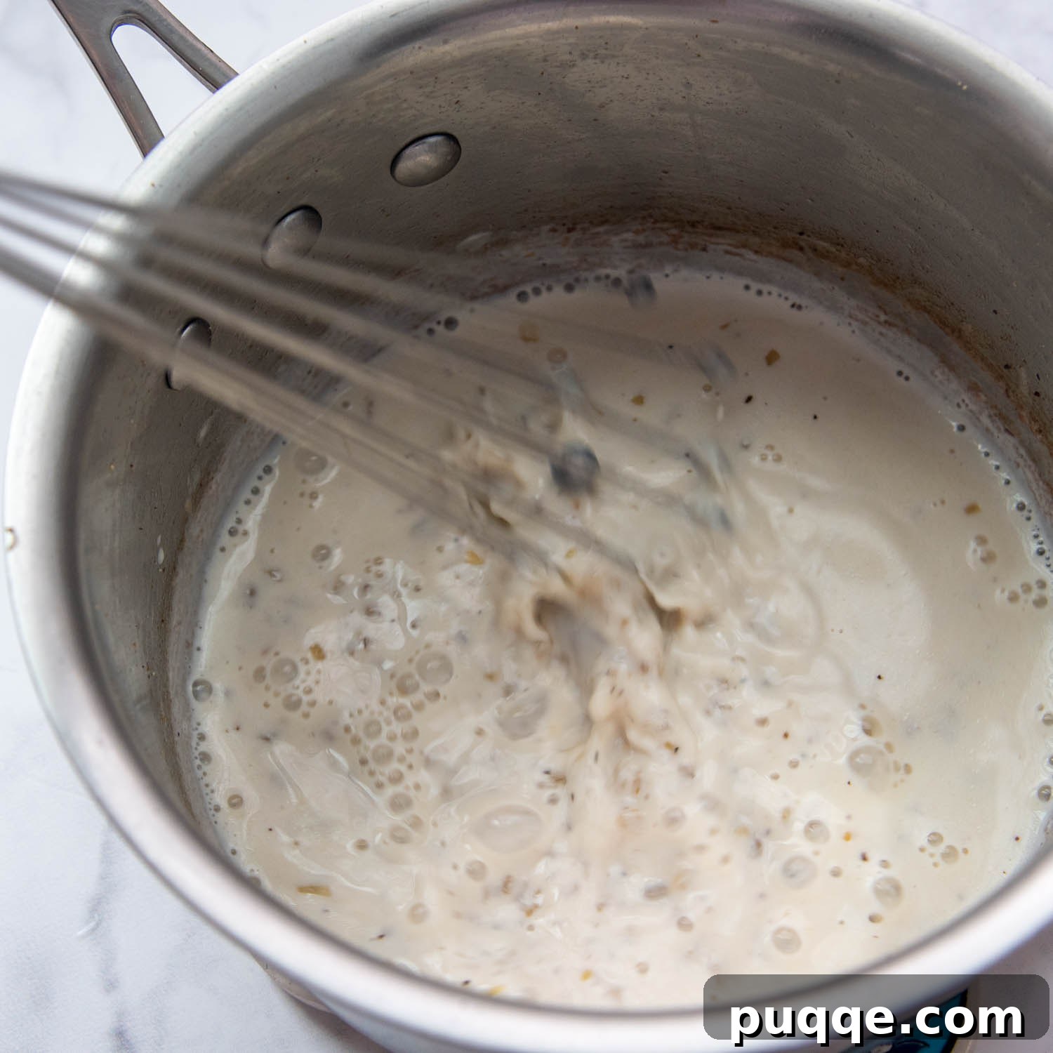 Velvety Fresh Spinach Artichoke Dip 4 A creamy white sauce being whisked gently in a saucepan on the stove, showing its smooth texture.