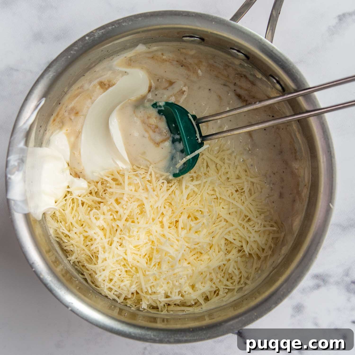 Velvety Fresh Spinach Artichoke Dip 6 Hands stirring freshly grated Parmesan cheese and sour cream into the white sauce in a saucepan.
